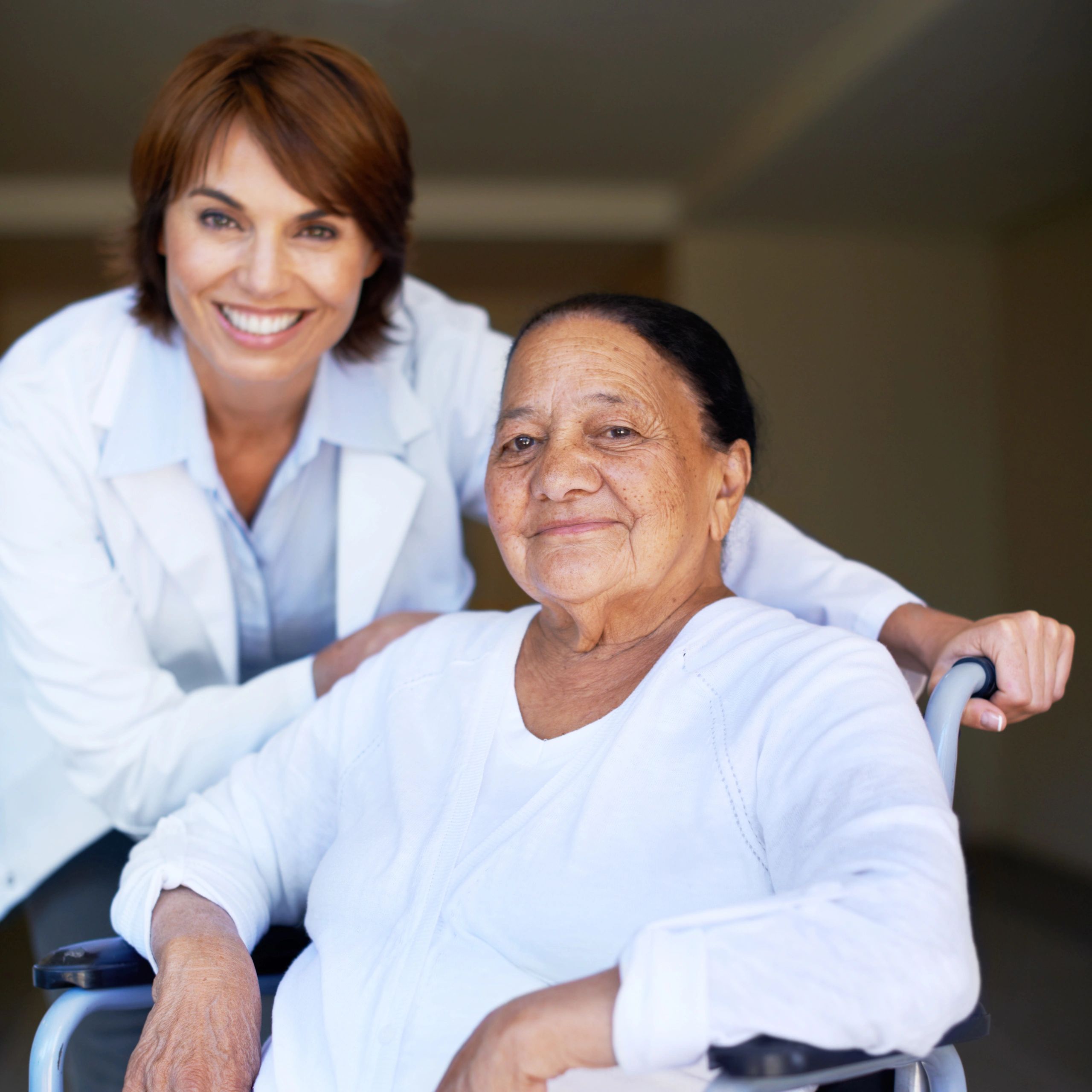 Caregiver in blue scrubs assisting an elderly patient in a wheelchair
